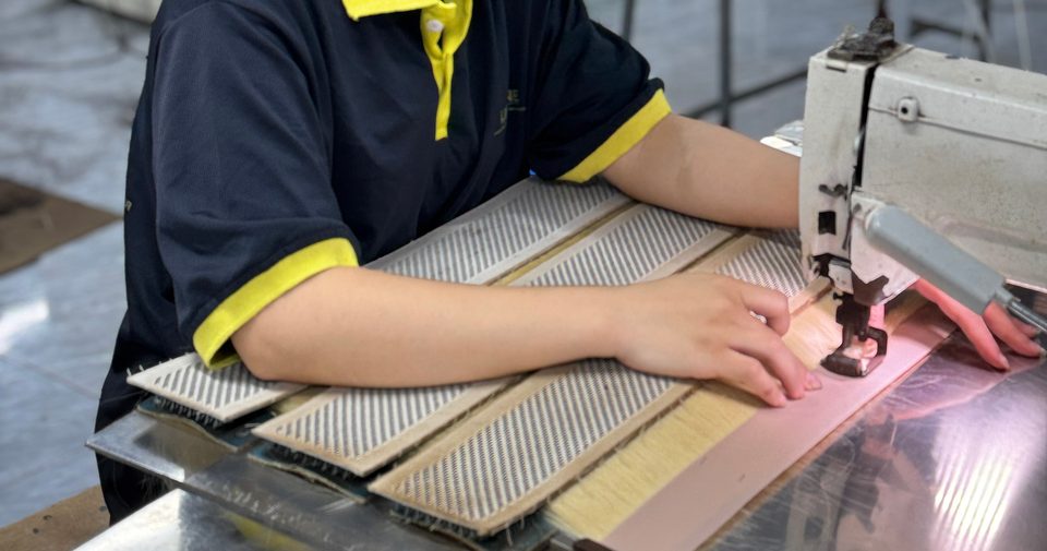 Hands guiding hair wefts through a sewing machine at the factory