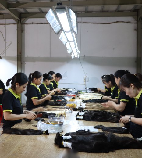 Workers sorting bundles of black hair at long tables