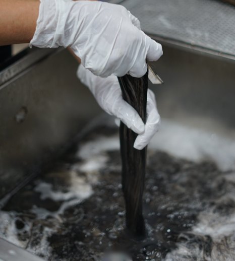 A gloved hand rinsing a hair bundle in a foaming wash tank