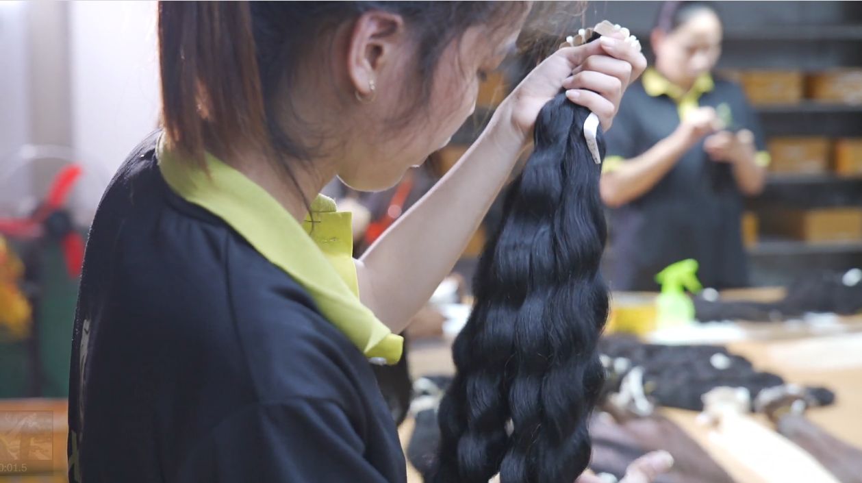 A Luxshine worker inspecting a batch of wavy hair