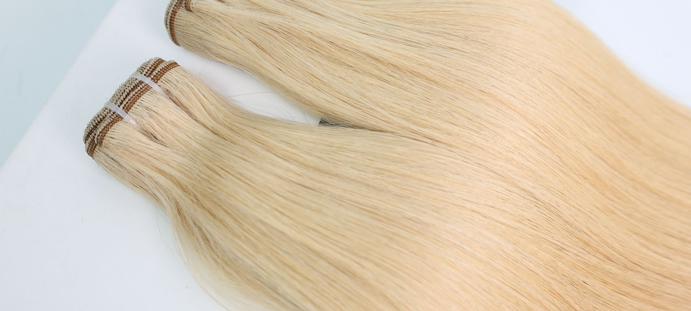 Two blonde Vietnamese Remy hair wefts laid on a white table, seen up close