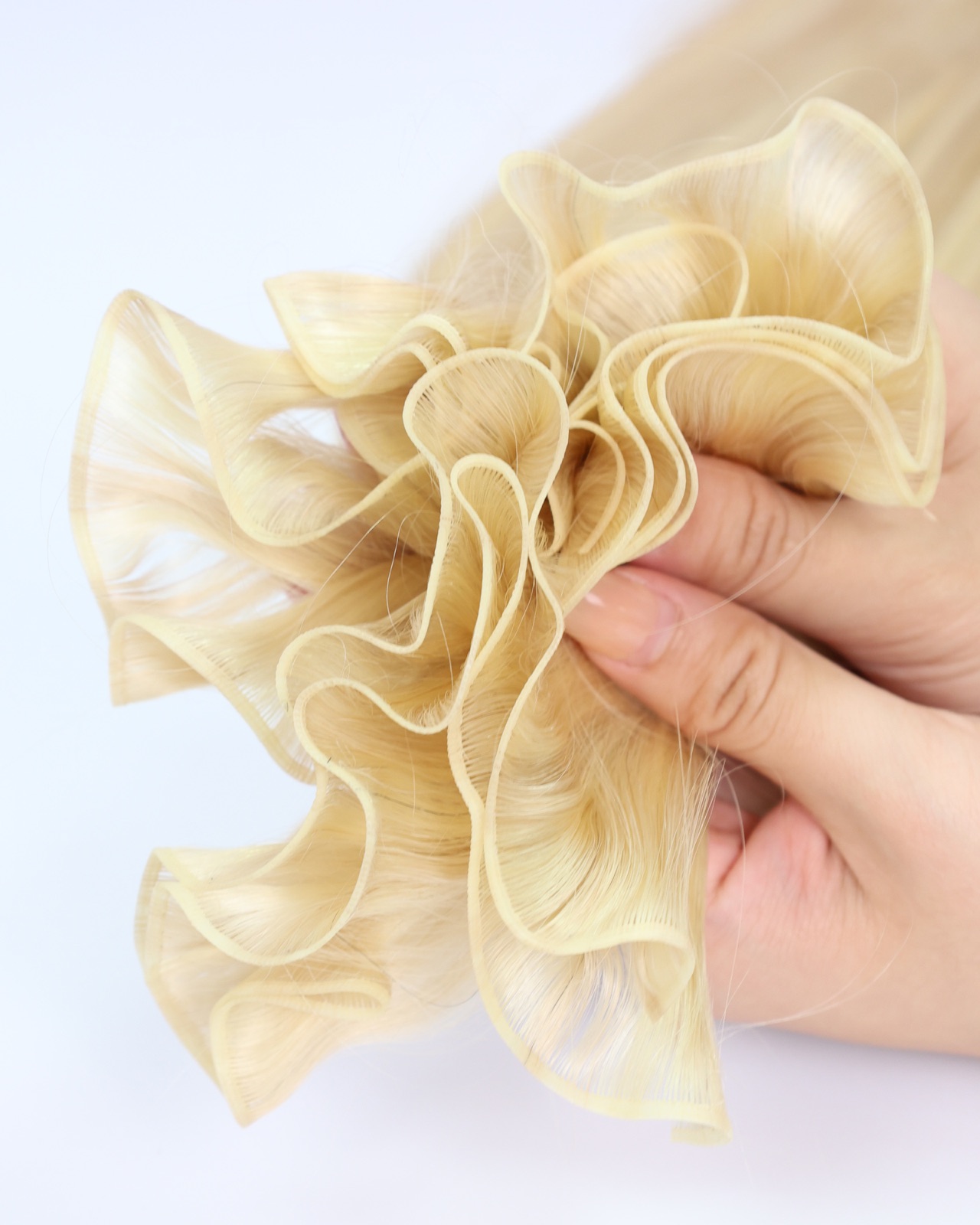 A blonde hair weft gathered into soft folds in one hand